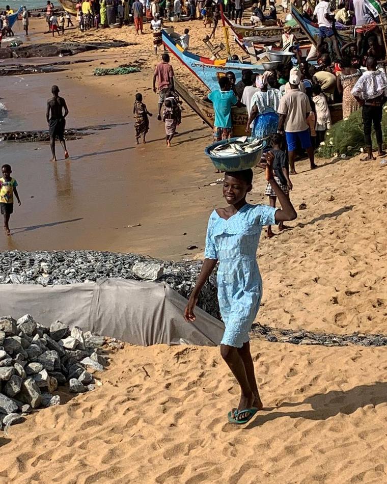 A girl carrying a basin of fish along a busy fishing beach